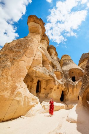 Téléchargez les photos : Young beautiful woman in red dress exploring Pasabag Monks valley in Cappadocia Turkey with unique rock formations and fairy chimneys - en image libre de droit