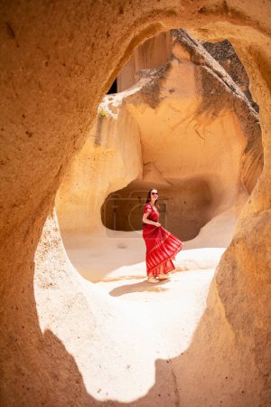 Téléchargez les photos : Young beautiful woman in red dress exploring Pasabag Monks valley in Cappadocia Turkey with unique rock formations and fairy chimneys - en image libre de droit