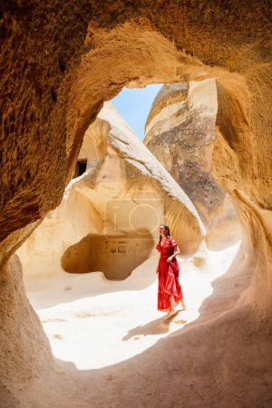 Foto de Young beautiful woman in red dress exploring Pasabag Monks valley in Cappadocia Turkey with unique rock formations and fairy chimneys - Imagen libre de derechos
