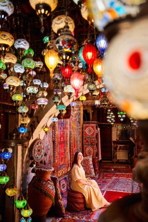 Photo for Beautiful woman in long yellow dress surrounded by colorful lanterns and carpets - Royalty Free Image
