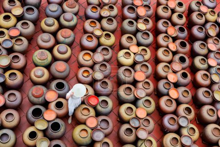 Photo for Top view of tourist woman wearing conical hat at soy sauce village in Hung Yen province in Vietnam with ceramics pots where soya beans are fermented - Royalty Free Image