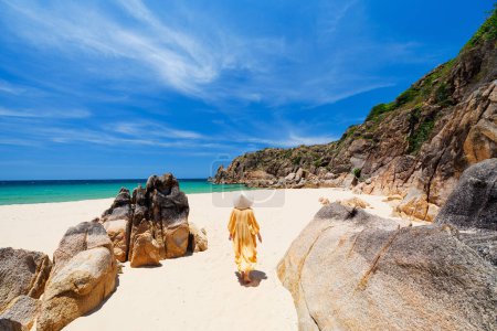 Photo for Young woman wearing yellow dress and conical hat on stunning white sand tropical beach in Vietnam enjoying vacation - Royalty Free Image