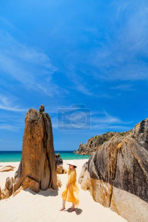 Photo for Young woman wearing yellow dress and conical hat on stunning white sand tropical beach in Vietnam enjoying vacation - Royalty Free Image
