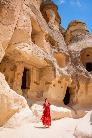 Foto de Young beautiful woman in red dress exploring Pasabag Monks valley in Cappadocia Turkey with unique rock formations and fairy chimneys - Imagen libre de derechos