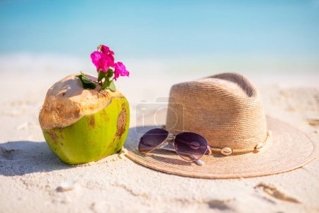 Foto de Sombrero de paja, gafas de sol y coco en una playa tropical de arena blanca - Imagen libre de derechos