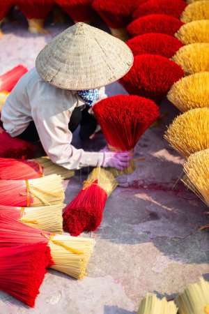 Foto de Trabajadora con sombrero cónico entre varillas de incienso rojo secándose al aire libre en la aldea cerca de Hanoi en Vietnam - Imagen libre de derechos