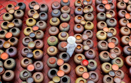 Photo for Top view of tourist woman wearing conical hat at soy sauce village in Hung Yen province in Vietnam with ceramics pots where soya beans are fermented - Royalty Free Image