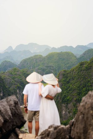 Foto de Hermosa pareja disfruta de viajar por el sudeste asiático contemplando las vistas de las montañas kársticas y el río de la Cueva de Mua en Vietnam. Enfócate en paisajes impresionantes. - Imagen libre de derechos