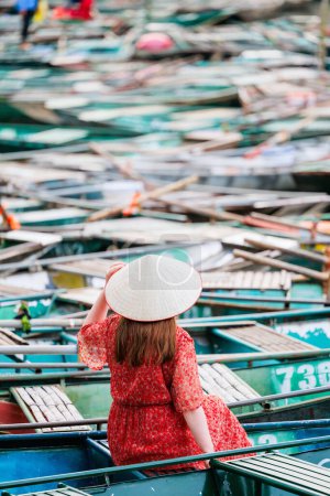 Rückansicht einer kaukasischen Frau, die den Blick auf hunderte Boote genießt, die am Pier von Tam Coc in Vietnam geparkt sind