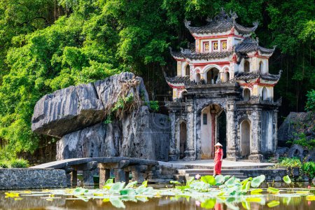 Beautiful woman wearing red dress and conical hat visiting Bich Dong pagoda in Ninh Binh Vietnam. Bich Dong Pagoda is a popular tourist destination of Asia.
