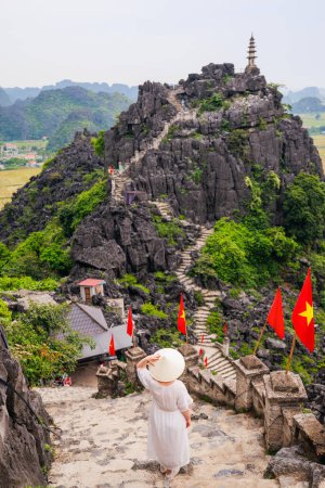 Photo for Back view of beautiful woman wearing white dress and conical hat enjoys stunning views of karst mountains of Mua Cave in Vietnam. - Royalty Free Image