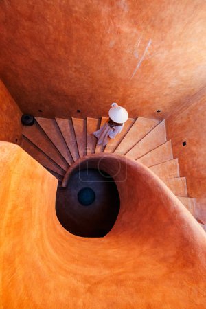 Beautiful woman wearing white dress and conical hat walking down spiral staircase