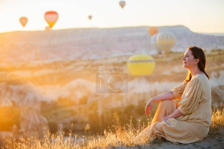 Foto de Young woman admire scenery of hot air balloons flying over Love valley with rock formations and fairy chimneys in Cappadocia Turkey - Imagen libre de derechos