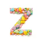 The capital letter is made of candies in the shape of Easter eggs on a white background.