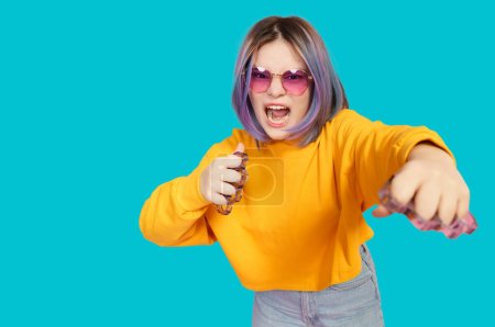 Angry teenager with brass knuckles hits camera on blue background. Pubertal journey of adolescence. . High quality photo