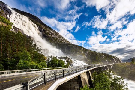 Téléchargez les photos : Énorme cascade puissante et rugissante de Langfossen sur la rivière Vaule. Le pont est clôturé avec des balustrades. Passe par l'autoroute. Journée froide et pluvieuse en été. Norvège occidentale. - en image libre de droit