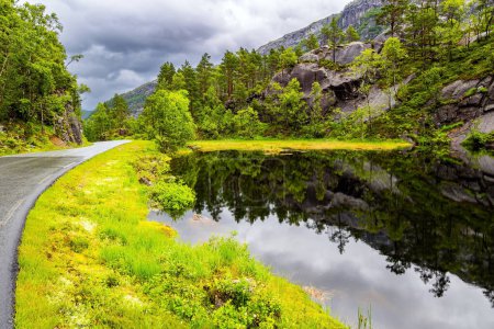 Foto de Pequeño lago tranquilo junto a la carretera. El pintoresco camino en Noruega. Viaje de verano al norte de Europa. Día de verano frío y lluvioso. Noruega Occidental. - Imagen libre de derechos