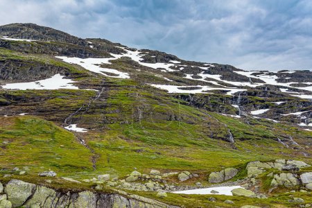 Foto de Las montañas sin árboles están cubiertas de campos de nieve, la nieve del año pasado. Viaje al oeste de Noruega. Camino escénico a Roldal. Frío día nublado de julio - Imagen libre de derechos