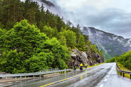 Foto de Motorcyclists passing by the waterfall. The Langfossen waterfall intersects with the highway and flows into the Acre Fjord. Majestic natural phenomenon. Summer cold day. - Imagen libre de derechos