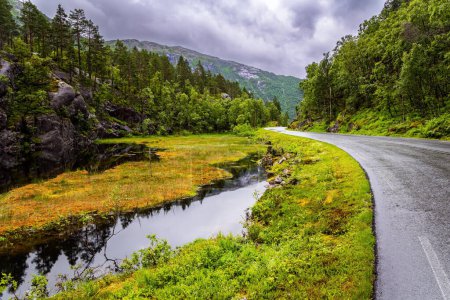 Foto de The picturesque road in Norway. Summer trip to the north of Europe. Summer cold and rainy day. Western Norway. Narrow fast shallow stream rumbles on the riffles - Imagen libre de derechos