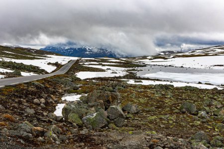 Foto de Gray clouds and fog. Great "Snow Road". Huge cold snowfields and sharp stone placers. Cold July in Northern Europe. Journey to the fabulous northern country of Norway. "Bjorgavegen" - Imagen libre de derechos