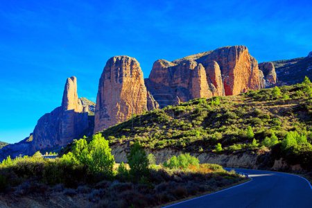 Téléchargez les photos : Asphalt highway passes through the rocks. The foothills of the Pyrenees. Sunny afternoon. The magnificent Mallets of Riglos is a conglomerate of rock formations. Romantic trip to Spain - en image libre de droit