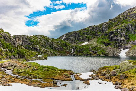 Photo for Large snowfields remained in the lowlands and on the slopes of the mountains. Ice lake surrounded by green mountains. Cold summer in Norway. Traveling on road 520. - Royalty Free Image