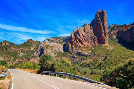 Photo for Asphalt highway passes through the rocks. The Mallets of Riglos. Part of the foothills of the Pyrenees. Hot sunny afternoon. Romantic trip to Spain. Aragon. - Royalty Free Image