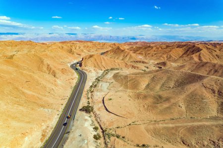 Dry waterless hills of yelloy and beige clay. Judean desert on the shores of the Dead Sea. Magnificent  highway curve picturesquely among the hills. Israel. Shooting from bird's eye view, from drone. 