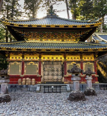 Photo for Sunset. Japan. Ornate temple with gilded roof. The rows of stone lanterns - sculptures. The temple and shrine of Nikko Tosho-gu is dedicated to the shogun Tokugawa Ieyasu. Building complex built in 1617. - Royalty Free Image