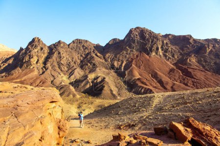 Frau in blauer Jacke fotografiert begeistert seltsame Felsen aus rot-orangefarbenem Sandstein. Bunte Landschaften. Die Eilat-Berge. Israel. 