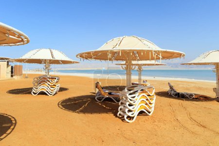 Téléchargez les photos : Chaises de plage empilées sur la plage. Mer Morte. Côte d'Israël. Beau parapluie rond protège du soleil. Le lac salé sans drainage au Moyen-Orient. - en image libre de droit
