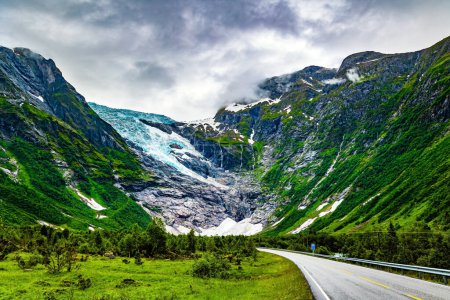 Foto de El glaciar más grande de Europa continental, Jostedalsbreen, se encuentra en las montañas. El frío verano en Noruega. La carretera serpentea a través de un hueco estrecho. Parque Nacional Jostedalsbreen. - Imagen libre de derechos