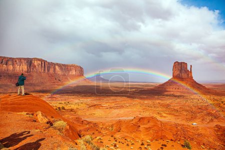 Tourist in Jacke fotografiert eine herrliche Landschaft. Die berühmten Felsfäustlinge. USA. Navajo-Indianerreservate. Monument Valley entsteht in Arizona und Utah. Der helle Regenbogen