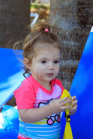 Téléchargez les photos : Adorable petite fille jouant sur la plage à l'ombre des palmiers. Bonne famille. Vacances en famille dans un hôtel sur l'île grecque de Chypre. Plage confortable sur la côte méditerranéenne. - en image libre de droit