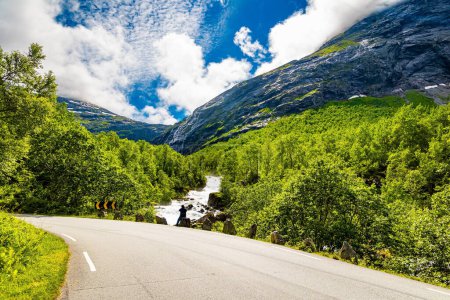 Travel to fabulous Scandinavia. Road to the famous Troll Staircase. Stormy rocky mountain stream flows among the majestic mountains. Norway. Woman taking pictures of landscape