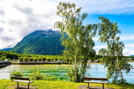 Téléchargez les photos : Magnifique temps ensoleillé en Norvège. L'immense lac est entouré de collines pittoresques arrondies. Il y a des bancs sur le talus du lac. Voyage en Scandinavie fabuleux - en image libre de droit
