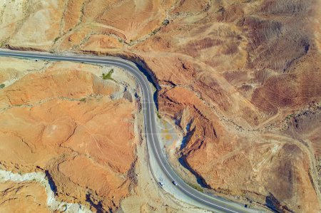 Dry waterless hills of yellow, beige and gray clay. Beautiful road curve among the hills. Judean desert on the shores of the Dead Sea. Shooting from a drone, Israel