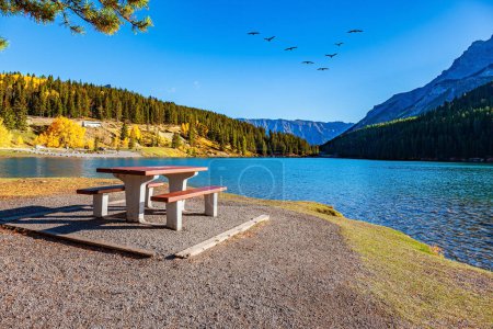 Rocky Mountains in Canada. Table and benches for picnic on the shore of Lake Two Jack. The cold water of the lake reflect the surrounding mountains. 