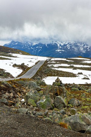 Great asphalt "Snow Road". Huge cold snowfields and sharp stone placers. Cold July in Northern Europe. Gray clouds and fog. Journey to the fabulous northern country of Norway.