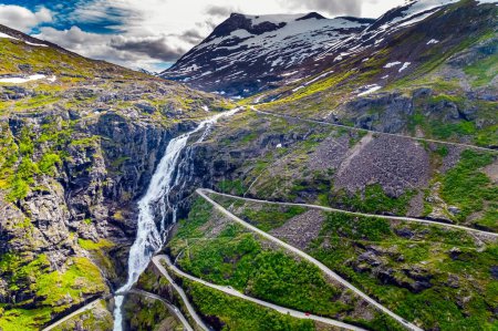 Téléchargez les photos : Trollstigen Norge / Troll Staircase / - l'endroit touristique le plus populaire en Norvège. L'énorme cascade de Stigfossen. La route serpentine serpente pittoresque sur les pentes verdoyantes du canyon - en image libre de droit