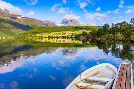 Téléchargez les photos : Masse en bois avec bateau. Lac peu profond Eidsvatnet dans les montagnes de Norvège. L'été en Scandinavie. L'eau reflète des nuages luxuriants, un ciel bleu et des rivages boisés. - en image libre de droit