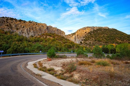 Téléchargez les photos : L'autoroute de l'asphalte passe entre des falaises escarpées. Le voyage en Espagne. Le ciel est couvert de nuages légers. - en image libre de droit