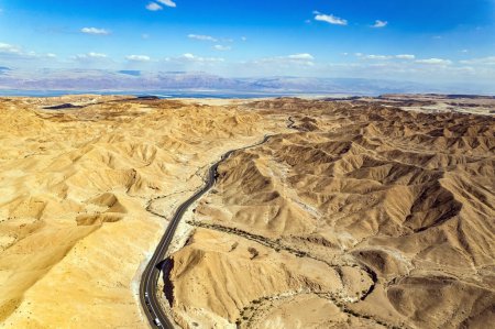 Desierto a orillas del Mar Muerto. La autopista del asfalto serpentea entre las colinas. El lodo del Mar Muerto tiene propiedades curativas. Vista de pájaro. Israel. 