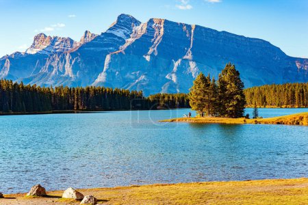 The little island overgrown with evergreen spruce trees. The cold emerald green water of the lake Two Jack reflect the surrounding mountains. Rocky Mountains in Canada. 