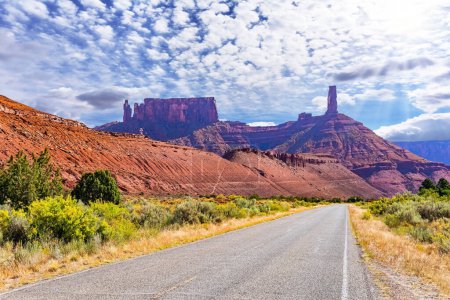 USA. Breite Asphaltstraße zwischen malerischen Hügeln und Felsen von bizarren Formen. Utah Red Sandstones. Die Rot- und Brauntöne der pulsierenden Landschaft Utahs
