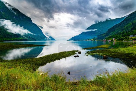 Swampy shores of the lake. Picturesque valley surrounded by high forested mountains. Cold summer in Norway. Jostedalsbreen Park. 