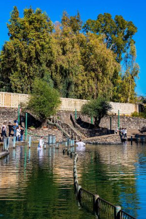 Foto de YARDENIT, ISRAEL - 21 DE ENERO DE 2023: Los peregrinos gozosos en camisas bautismales reciben el bautismo en el río Jordán. Yardenit es un centro de bautismo para católicos y cristianos ortodoxos. - Imagen libre de derechos