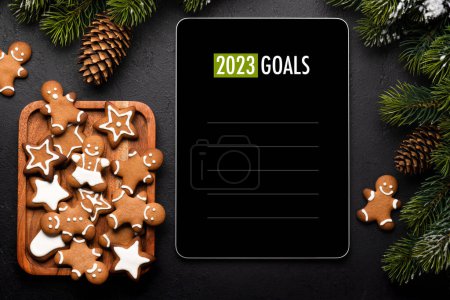 Téléchargez les photos : Tablette avec le modèle d'objectifs de l'année prochaine, biscuits au pain d'épice et décor de Noël. Modèle d'écran de l'appareil de Noël - en image libre de droit