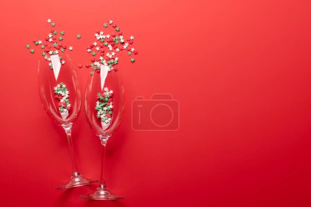 Foto de Tarjeta de San Valentín con copas de champán y dulces en forma de estrella. Sobre fondo rojo con espacio para tus saludos - Imagen libre de derechos
